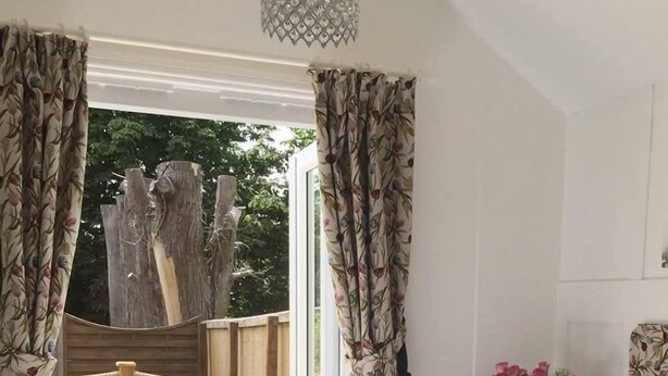 A bedroom with a bed, a small table with chairs, a vase with flowers, and a view of the outdoors. - Clarence House Holidays (Shanklin)