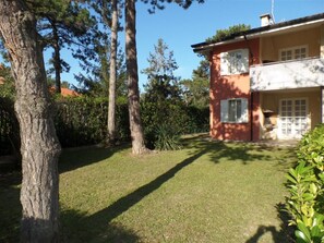 Ein Haus mit gepflegtem Rasen, einem großen Baum und einem zweistöckigen Gebäude mit Balkon.