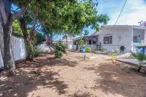 A residential area with a dirt path, a large tree, and white houses with balconies. - Cozy apartment (Oranjestad)