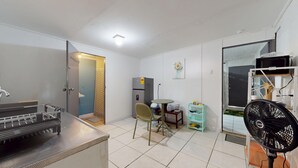 Ein kompakter Wohnraum mit einer Küchenzeile, einer Essecke mit Tisch und Stühlen, einem Kühlschrank, einem Ventilator und einem Fenster.