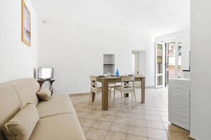 Una sala de estar con sofá, una mesa de comedor con sillas, televisor y lavadora.
