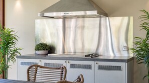 Une cuisine équipée d’une hotte en acier inoxydable, d’une plante en pot et d’un barbecue encastré.