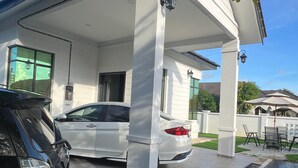 A covered carport with a white car parked inside, a black car parked outside, and a patio area with outdoor furniture.