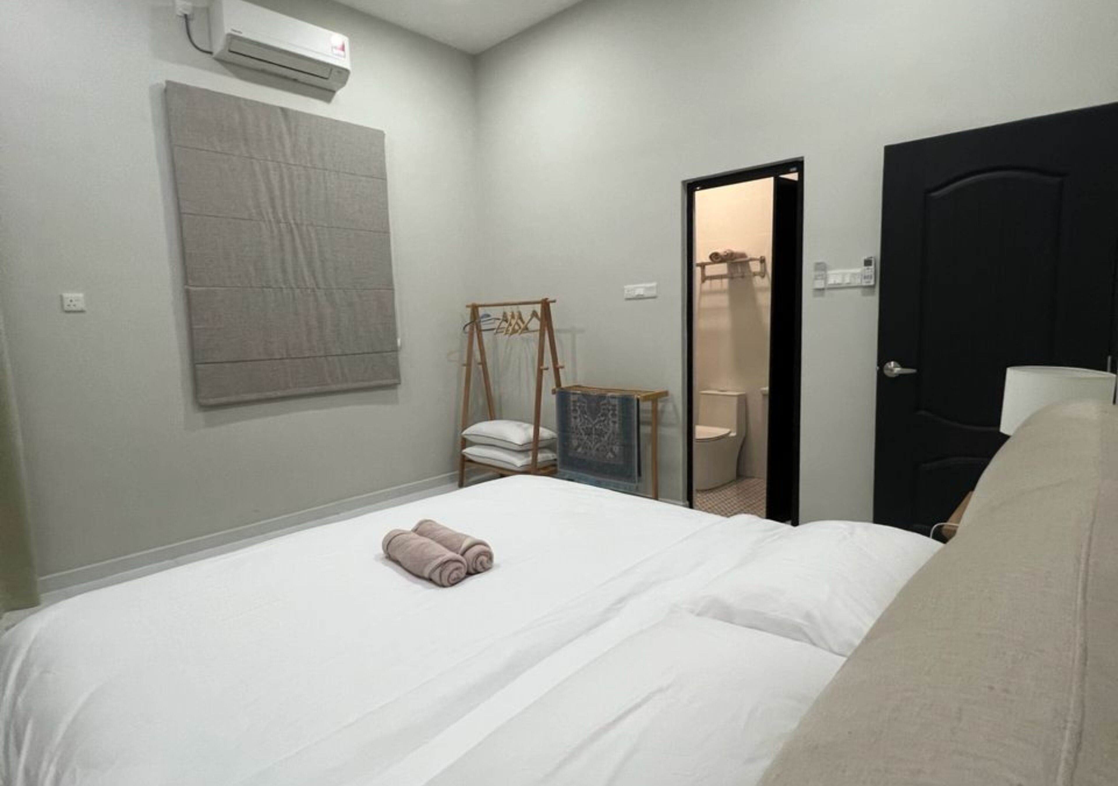 A hotel room with a bed, a wardrobe, a small seating area, and a door leading to a bathroom.