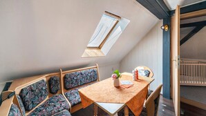 Une pièce chaleureuse avec un plafond en pente, une lucarne, une table en bois ornée d’un vase, des coussins à motifs et un berceau.