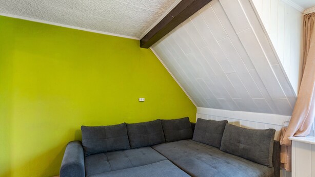 A room with a green wall, a grey sofa, and a sloped ceiling. - Apartment 'Olivias' with Shared Pool, Shared Garden and Wi-Fi (Thürkow)