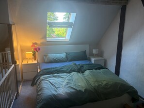 Ein Schlafzimmer mit einem Bett, einem Nachttisch, einer Lampe, einem Fenster und einem Babybett.
