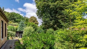 A garden with a brick building, a wooden pergola, and various green plants. - Apartment 'Olivias' with Shared Pool, Shared Garden and Wi-Fi (Thürkow)