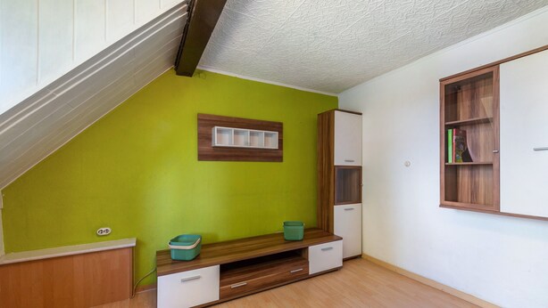 Une pièce avec un plafond en pente, un mur vert, un banc en bois doté de tiroirs, une armoire blanche et une bibliothèque en bois.