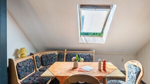 A small, cozy room with a sloped ceiling and a skylight. There is a wooden table with a patterned tablecloth, a chair, and a small potted plant. - Apartment 'Olivias' with Shared Pool, Shared Garden and Wi-Fi (Thürkow)