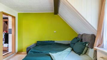 Ein Schlafzimmer mit grüner Wand, einem Bett mit vielen Kissen und einem Fenster mit Vorhängen.