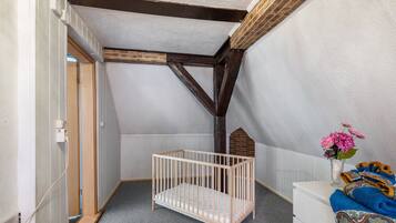 Ein Zimmer mit schrägen Wänden, einem hölzernen Babybett, einer weißen Kommode und einer Vase mit Blumen.