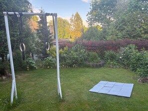 Um jardim gramado com baloiço de metal e trampolim.
