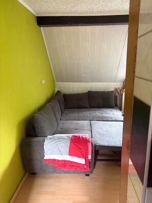 Quarto de canto com sofá seccional cinza, uma mesa pequena e parede verde.