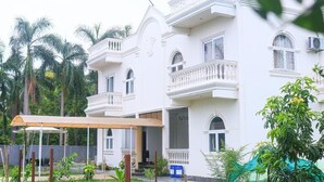 A white multi-story building with balconies, surrounded by greenery.