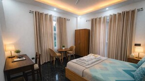 A hotel room with a bed, a desk, a chair, a small table, a wardrobe, and curtains.