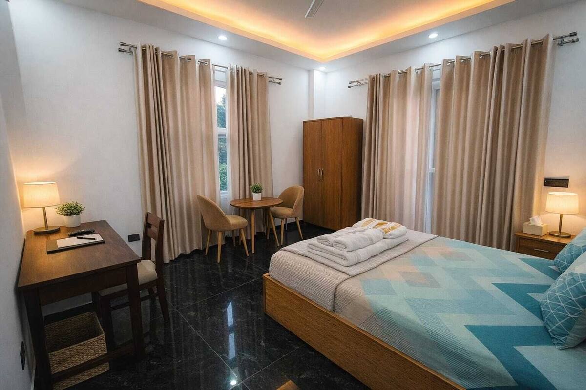 Une chambre d’hôtel comprenant un lit, un bureau, une chaise, une petite table, une armoire et des rideaux.