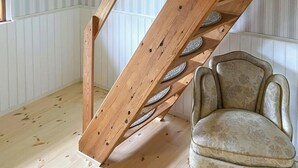 Una habitación con una escalera de madera, una silla y un muro blanco con paneles.