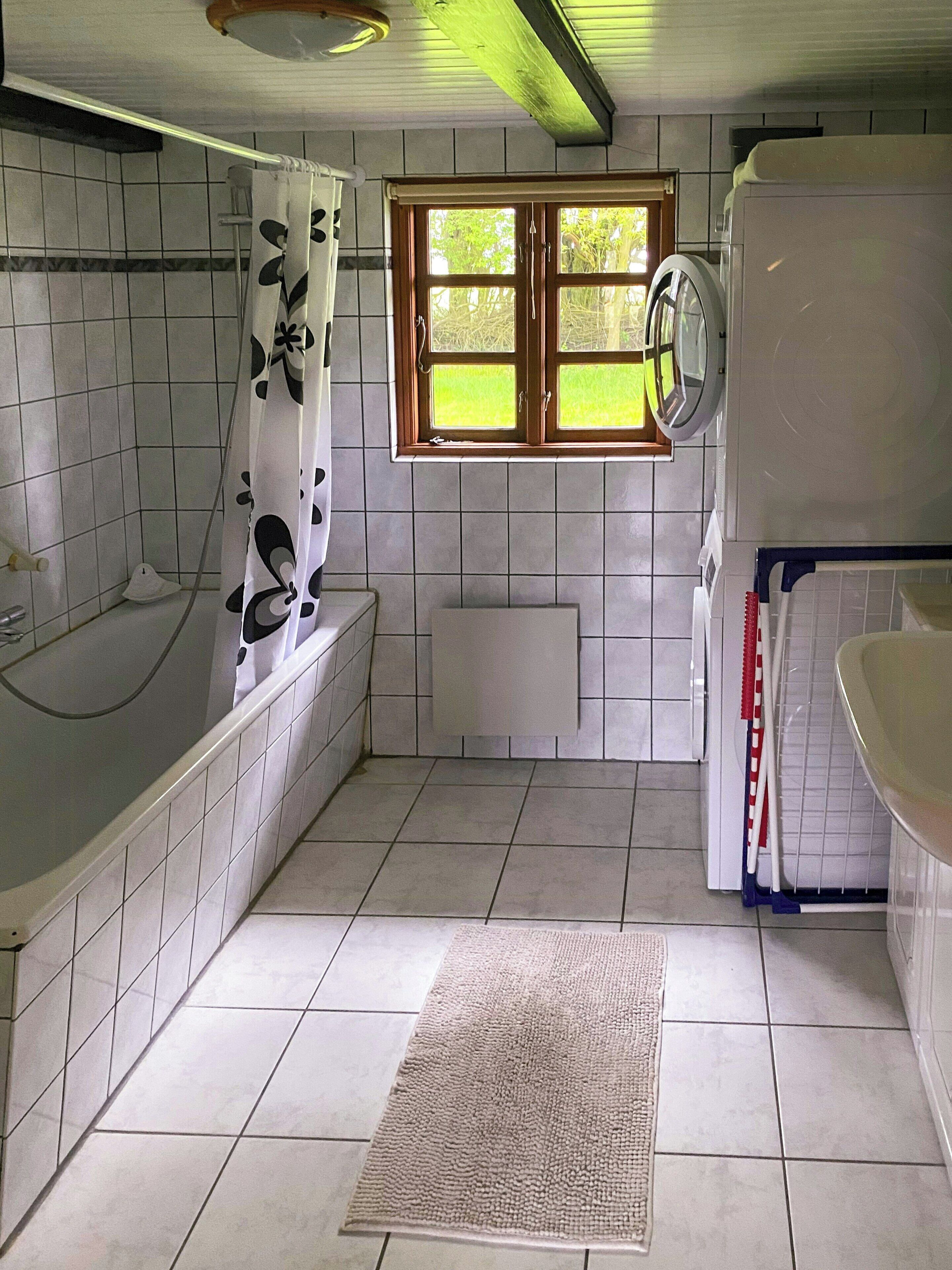 Ein Badezimmer mit Badewanne, Fenster, Heizkörper und Waschmaschine.