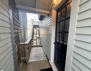 A narrow exterior corridor with a wooden staircase leading to a door. - Charming 3 Bedroom Apartment . Walk to Ferry, Shops & Beach (Tisbury)