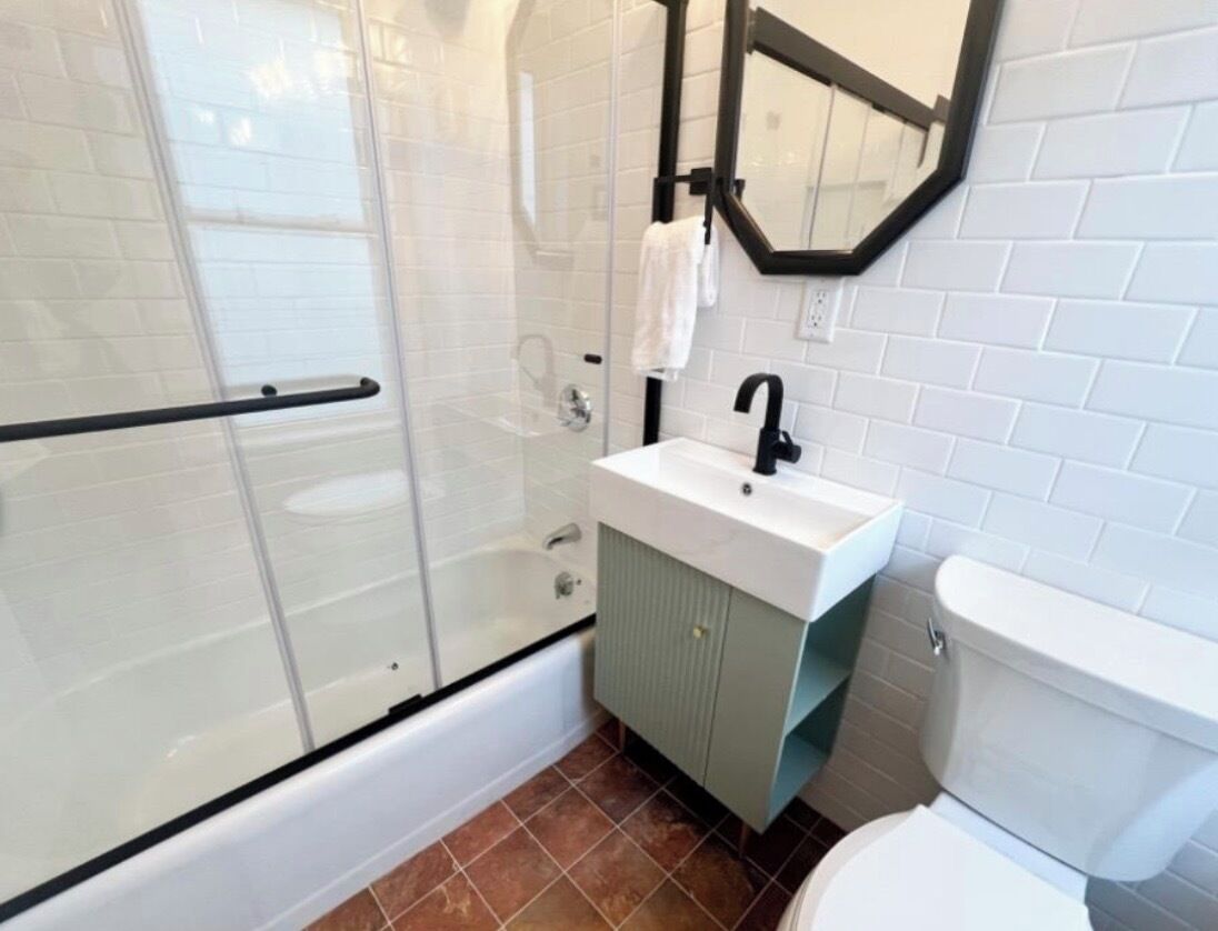 A bathroom with a glass shower enclosure, a white sink, a toilet, and a mirror above the sink.