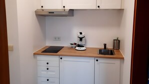 A compact kitchen with white cabinets, a wooden countertop, a built-in stove, a coffee maker, and a sink.