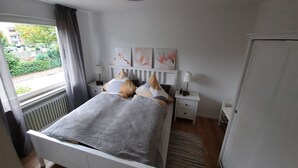 A bedroom with a bed, bedside tables, a radiator, a window with curtains, and artwork on the wall.
