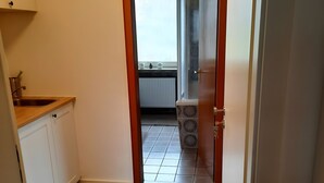A narrow hallway leading to a room with a radiator, a window, and a door with a frosted glass panel.