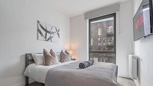 Ein Schlafzimmer mit Bett, Wandfernseher, Fenster und Heizkörper.