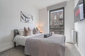 Un dormitorio con cama, televisor montado en la pared, ventana y radiador.