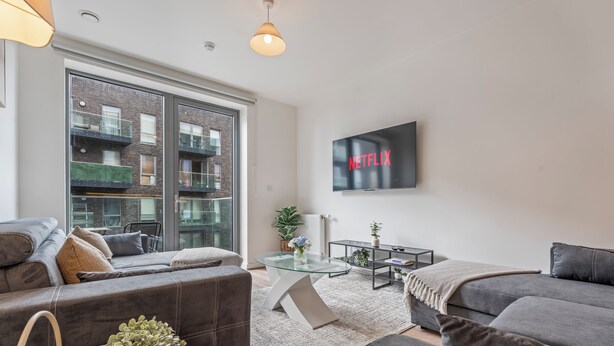 Ein modernes Wohnzimmer mit einem grauen Sofa, einem Glastisch und einem Fernseher, der 'NETFLIX' anzeigt.