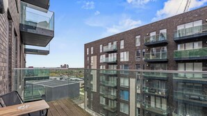 Ein Balkon mit Tisch und Stühlen, mit Blick auf ein modernes Gebäude mit mehreren Balkonen und Fenstern.