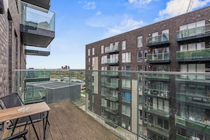 A balcony with a table and chairs, overlooking a modern building with multiple balconies and windows. - Stylish 2BR Wembley Stay |Sleeps 8| 5-Min Walk to Stadium (London)