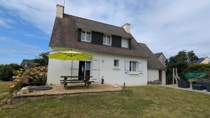 Ein zweistöckiges Haus mit einer Terrasse, einer Bank und einem gelben Sonnenschirm.