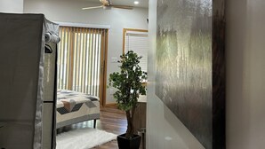 Un interior moderno con un ventilador de techo, un cuadro abstracto grande, una planta en maceta y una cama con colcha estampada.