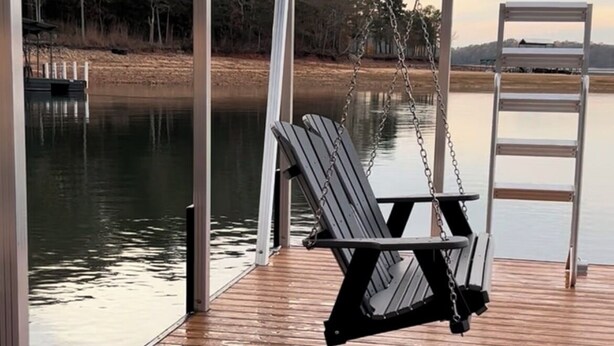 Una terraza de madera con una silla colgante y una escalera, con vista a un cuerpo de agua tranquilo y árboles.