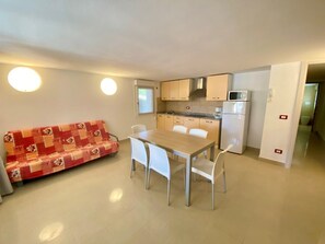 Ein kompakter Wohnraum mit Küchenzeile, einer Essecke mit Tisch und Stühlen sowie einer Couch.