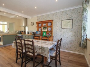 Uma sala de jantar com uma mesa, cadeiras, um armário de madeira com pratos e um relógio na parede.