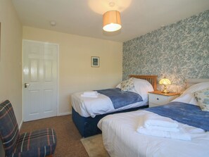 Ein Schlafzimmer mit zwei Betten, einem Sessel, einer Tür und einer Wand mit Blumenmuster-Tapete.
