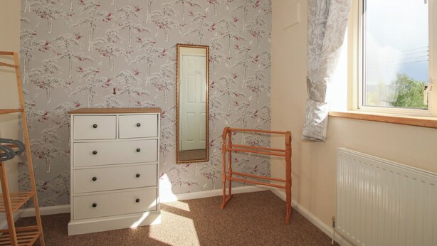 Een slaapkamer met een dressoir, een spiegel, een radiator en een raam met gordijnen.
