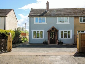 Une maison à deux étages avec une porte d’entrée, un petit porche et une allée menant à une entrée fermée par un portail.