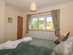 A bedroom with a bed, a window with curtains, a radiator, and a door. - Onny Views (Craven Arms)