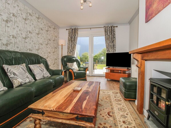 A living room with a green sofa, a wooden coffee table, a television, and a fireplace. - Onny Views (Craven Arms)