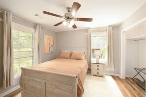 A bedroom with a bed, a ceiling fan, a window, a nightstand, and a chair.