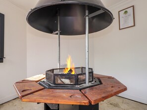 A wood-burning stove with a metal frame and a black top, placed on a wooden platform with a fire burning inside.
