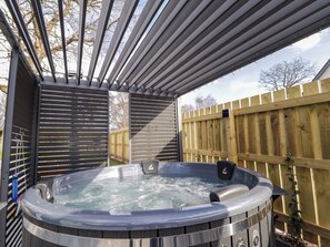 Un jacuzzi bajo una pérgola con una valla de madera al fondo.
