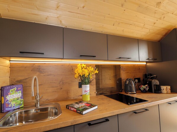 A modern kitchen with wooden cabinets, a stainless steel sink, a coffee machine, and a book titled 'A Cook's Tour of Scotland'.
