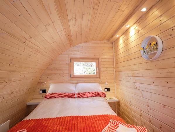 A cozy wooden room with a bed, a window, and a wall-mounted mirror.