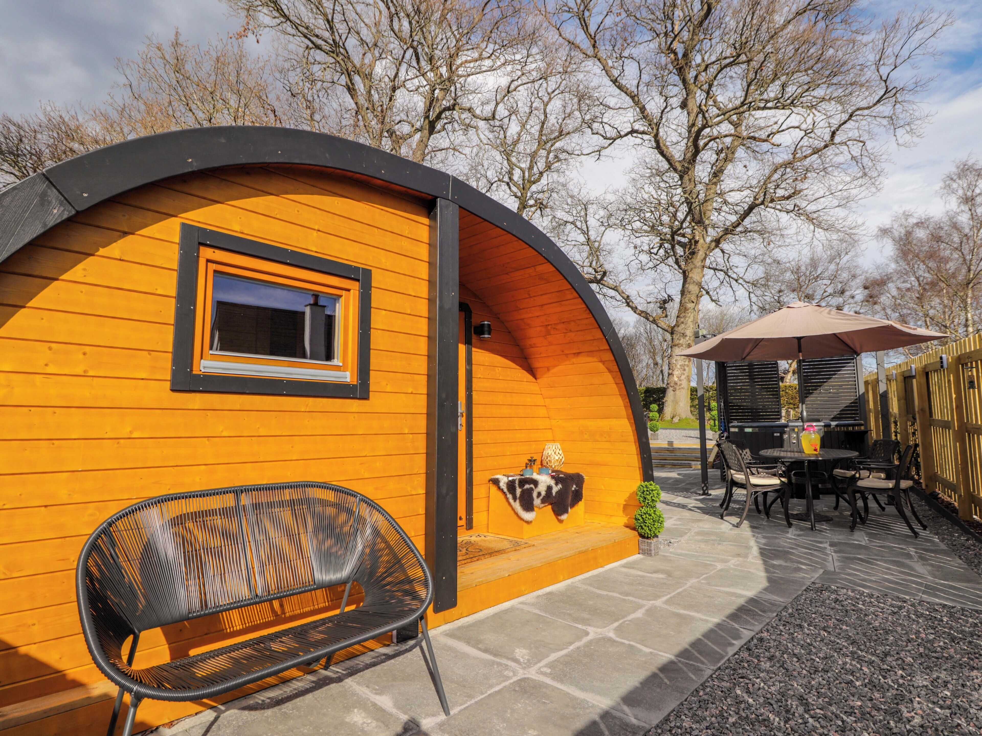 A cozy, wooden cabin with a curved roof, a window, a bench, and a small table with an umbrella.