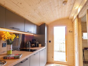 A modern kitchen with wooden ceiling, grey cabinets, a built-in stove, and a window leading to a balcony. - Little Oaks (Dingwall)